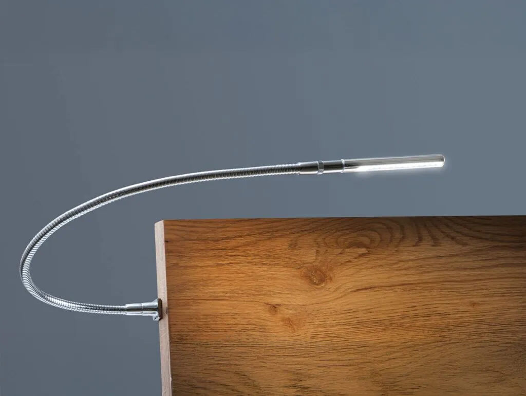 Eine moderne, biegsame Schwanenhals-LED-Lampe ist an der Kante einer hölzernen Oberfläche befestigt und beleuchtet das Holz vor einem schlichten grauen Hintergrund.