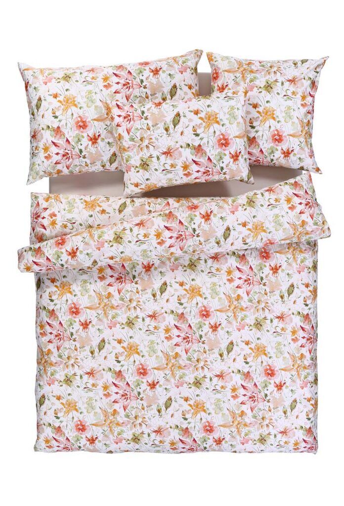 Ein sauber arrangiertes Bettset mit einem Blumenmuster aus orangefarbenen, rosafarbenen und gelben Blumen und grünen Blättern auf weißem Hintergrund, einschließlich zweier Kissen und einer Bettdecke.