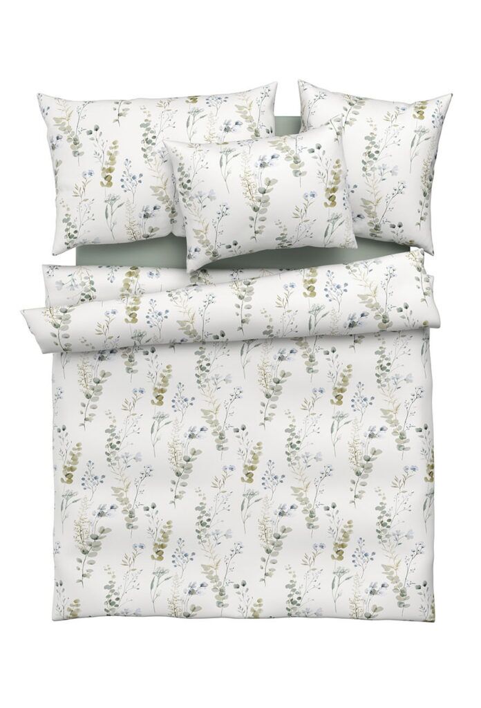 Ein sauber gemachtes Bettset mit einem weißen Bettbezug, Kissenbezügen und Laken, die alle ein zartes Blumenmuster in Grün-, Gelb- und Blautönen aufweisen. Das Design umfasst botanische Illustrationen von Blättern und Blumen.