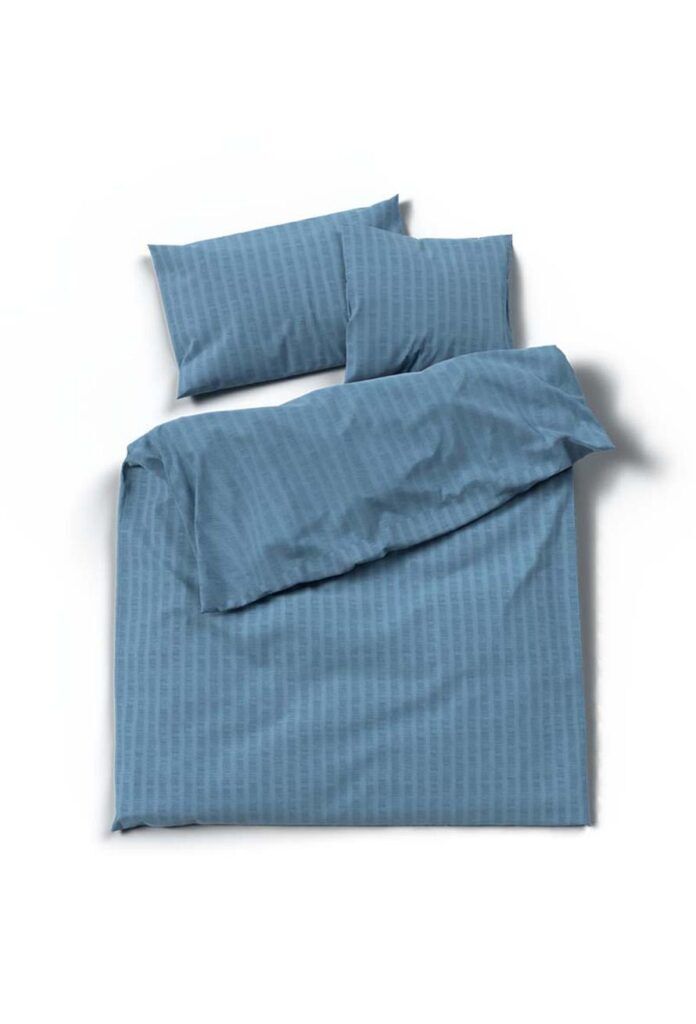 Ein ordentlich gemachtes Bett mit blauem Bettwäsche Satin Seersucker, mit dezenten Streifen auf dem Bettbezug und zwei passenden Kissen, vor einem schlichten weißen Hintergrund.