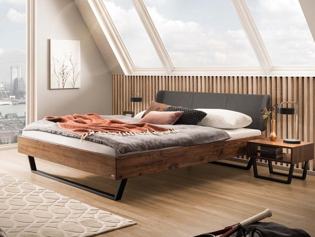 Ein modernes Schlafzimmer mit einem Holzpritschenbett, grauer Bettwäsche und einer orangefarbenen Decke. Große Fenster lassen natürliches Licht herein und bieten einen Blick auf die Stadt. Das Zimmer hat holzvertäfelte Wände, einen Nachttisch und eine minimalistische Einrichtung.