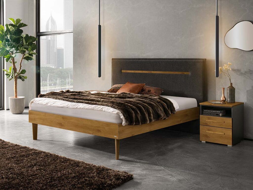 Ein modernes Schlafzimmer mit einem Holzbett mit dunklem Polsterkopfteil, braunem Bettzeug, einem Nachttisch mit Schubladen, einer Topfpflanze, Hängelampen, einem braunen Teppich und einem großen Fenster mit Stadtblick.