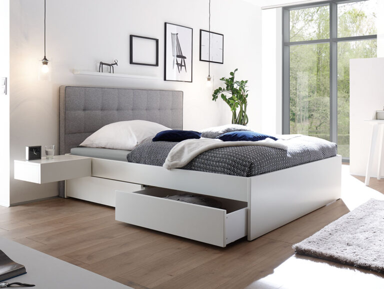 Modernes Schlafzimmer mit einem Hasena Schubladenbett "Function and Comfort Elito 2", mit Stauraumschubladen, grauem getuftetem Kopfteil, minimalistischem Dekor, großen Fenstern, sauber gemachter Bettwäsche und hellem Holzfußboden.