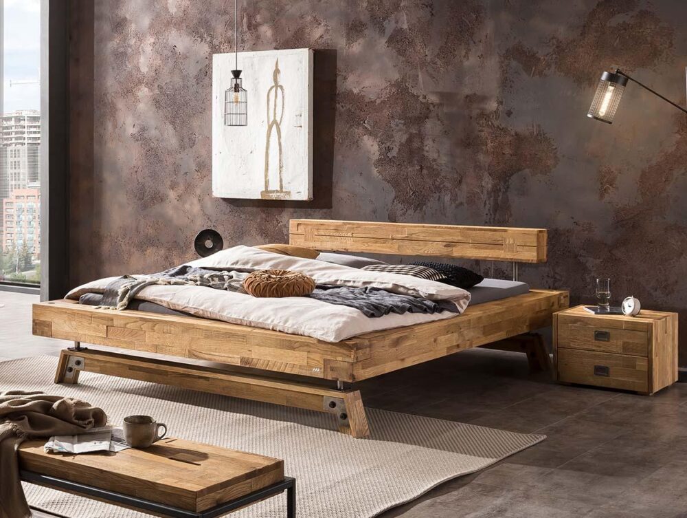 Ein modernes Schlafzimmer mit einem Holzbett mit neutraler Bettwäsche, einem kleinen Nachttisch, einer Bank und einer Beleuchtung im Industriestil an einer braunen, strukturierten Wand. Durch das Fenster auf der linken Seite ist eine Stadtlandschaft zu sehen.