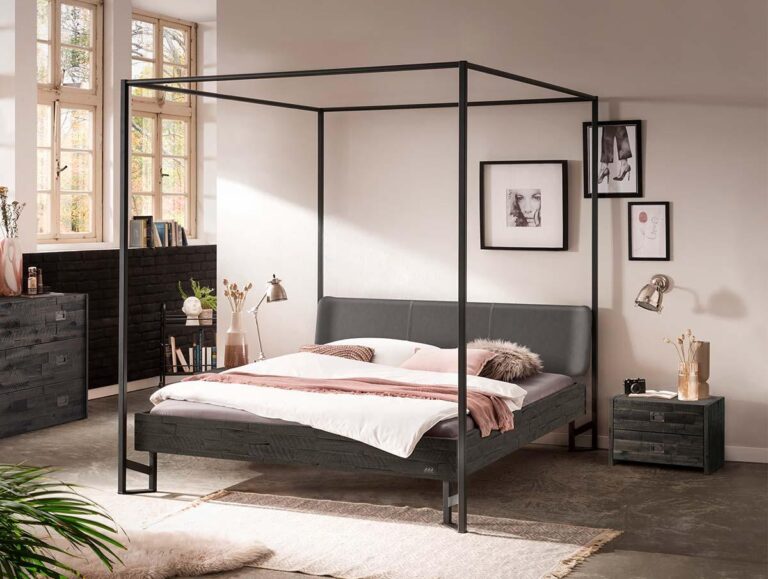 Ein modernes Schlafzimmer mit einem schwarzen Metall-Himmelbett, einem grauen Kopfteil, weißer und rosa Bettwäsche, einem Nachttisch mit Dekoration, Wandkunst, einer Lampe und großen Fenstern, die natürliches Licht hereinlassen.