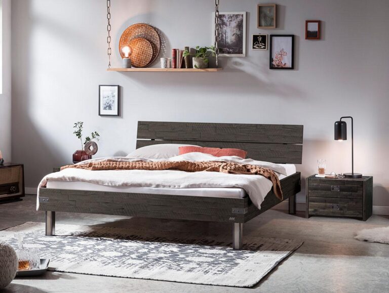 Ein modernes Schlafzimmer mit einem dunklen Holzbett, weißer Bettwäsche, einer braunen Decke, einem Nachttisch mit einer Lampe, Dekoration an der Wand und im Regal und einem gemusterten Teppich auf einem Betonboden. Die warme Beleuchtung schafft eine gemütliche Atmosphäre.