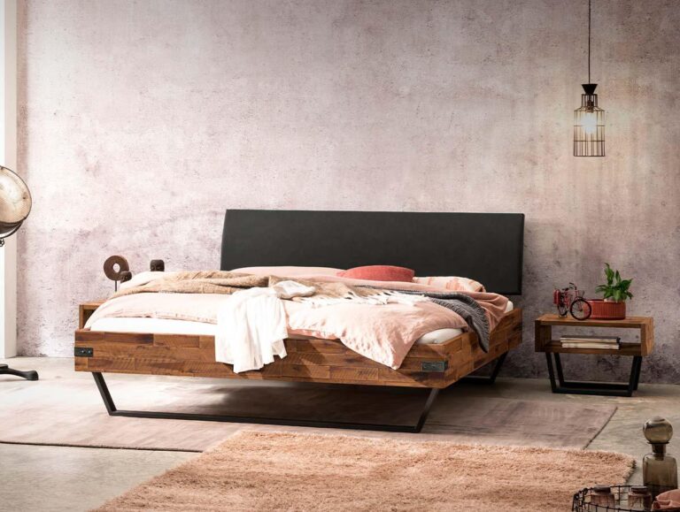 Ein gemütliches Schlafzimmer mit einem hölzernen Bettgestell, einem schwarzen Kopfteil, rosa und beiger Bettwäsche, einem passenden hölzernen Nachttisch, einer Industrielampe und minimalem Dekor vor einer hellen, strukturierten Wand.