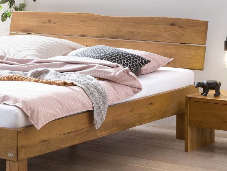 Ein Holzbett mit hellrosa Laken und Kissen, daneben ein hölzerner Nachttisch mit einer kleinen schwarzen Bärenfigur und einer Hängelampe in einem minimalistischen, modernen Schlafzimmer.