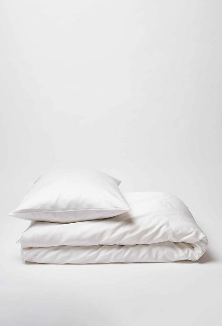 Ein fein säuberlich gestapeltes weißes Kissen und eine gefaltete weiße Bettdecke aus der Bettwäsche Journey Living Braga Snow-Kollektion stehen vor einem schlichten weißen Hintergrund.
