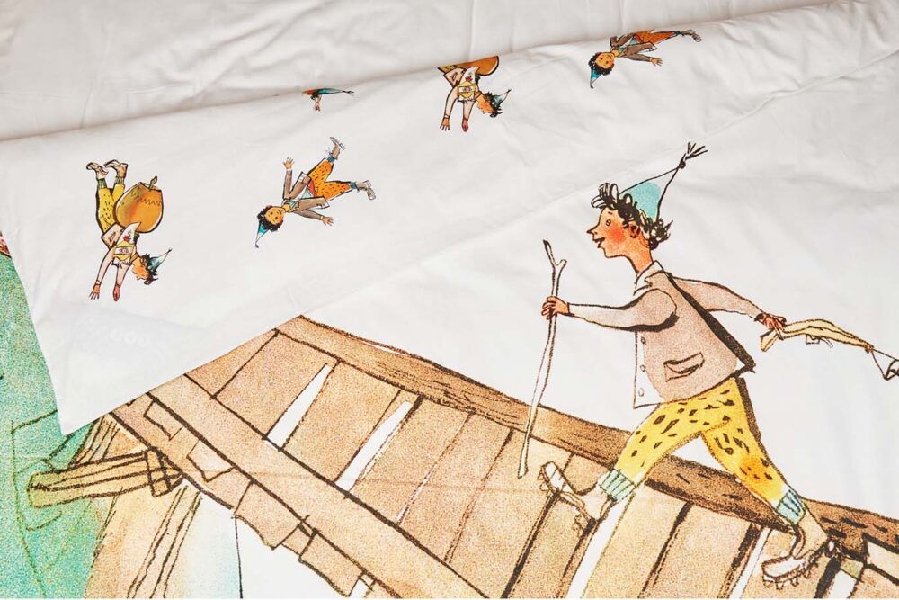 Der Bettwäsche Schellenursli Aufzug zeigt ein Kind in gelber Hose, blauem Hut und Jacke, das auf einer Holzbrücke geht, und darüber kleinere Bilder desselben Kindes in verschiedenen Posen.