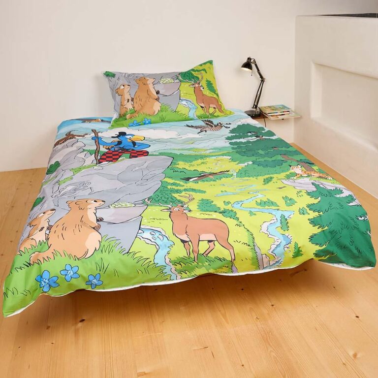 Ein Kinderbett ist in Bettwäsche Globi Nationalpark gekleidet, mit Cartoon-Tieren, einer Naturszene mit Rehen, Eichhörnchen, Bäumen, einem Bach und einer Kletterfigur. In der Nähe befinden sich das passende Kissen, das Buch und die Lampe.