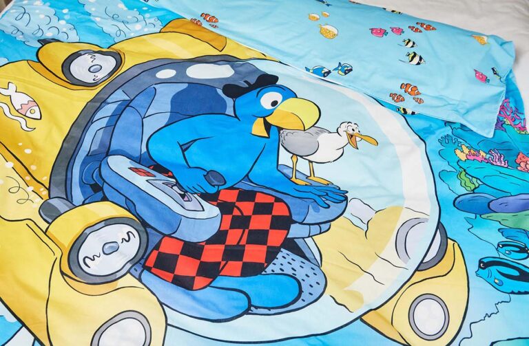 Bettwäsche Globi Ozean zeigt einen blauen Vogel in einem gelben U-Boot mit einer Möwe, umgeben von Unterwasserszenen, Fischen und Korallenriffen. Der Kissenbezug zeigt kleine Fische auf hellblauem Hintergrund.