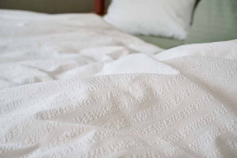 Nahaufnahme eines ordentlich gemachten Bettes mit strukturierter weißer Bettwäsche Journey Living Kemeri und einem knackigen weißen Kissen, das einen sauberen und einladenden Look erzeugt.