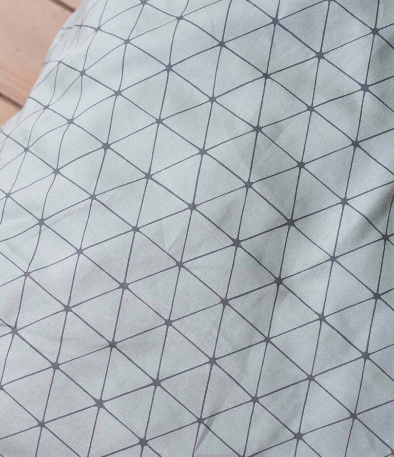 Eine Nahaufnahme von Bettwäsche Journey Living Peniche zeigt das geometrische Muster mit sich kreuzenden schwarzen Linien, die ein dreieckiges Gitter auf hellgrauem Hintergrund bilden.