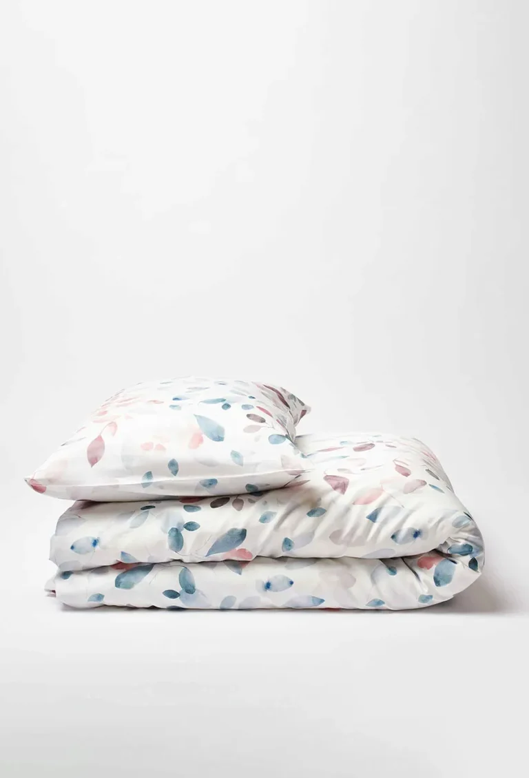 Eine ordentlich gefaltete Bettwäsche Journey Living Greina und ein Kissenbezug mit abstrakten Blättern in Pastellblau, -rosa und -beige sind vor einem schlichten weißen Hintergrund platziert.