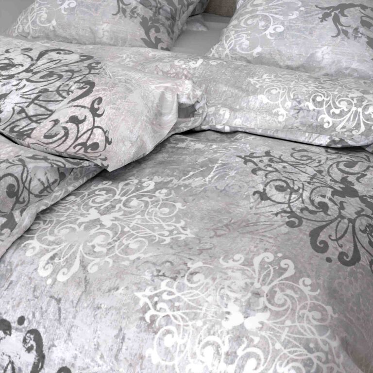 Die Nahaufnahme eines Bettes mit Bettwäsche Santiago Lotus Création zeigt vier Kissen und einen Bettbezug, die alle mit komplizierten grauen, schwarzen und weißen Wirbelmustern versehen sind und einen perfekt abgestimmten Look ergeben.