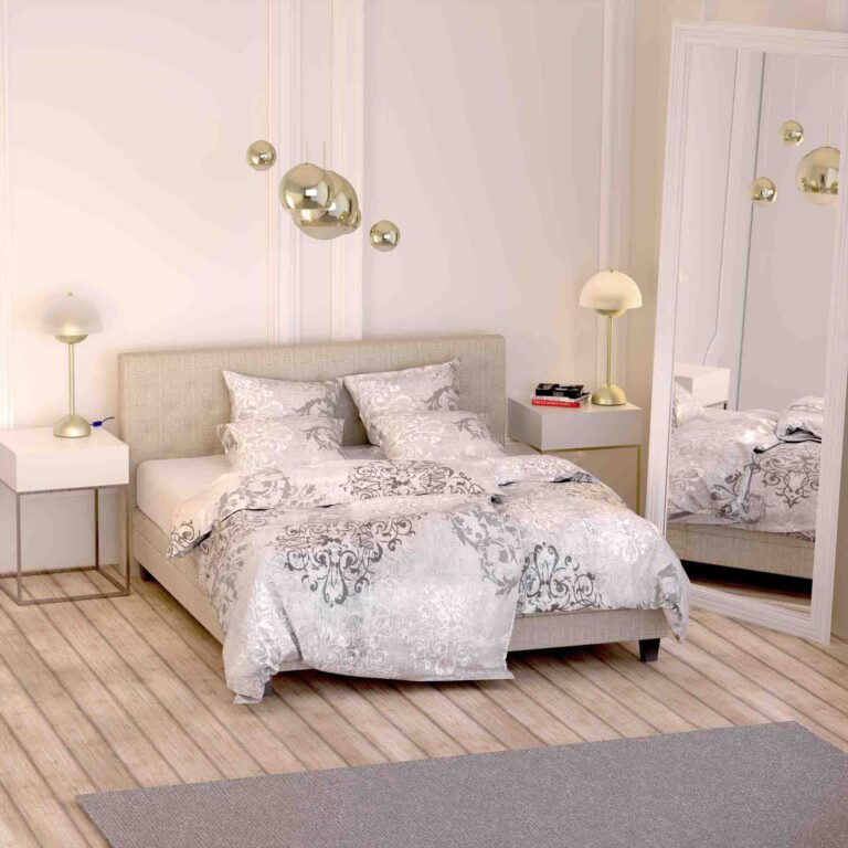 Ein modernes Schlafzimmer mit einem großen Bett mit Bettwäsche Santiago Lotus Création in Weiß und Grau, zwei Nachttischen mit Lampen, goldenen Wandleuchten, einem grauen Teppich und einem hohen Spiegel, der den stilvollen Raum reflektiert.