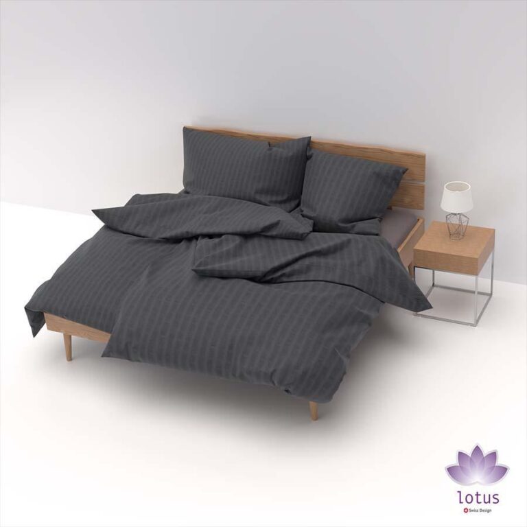 Ein ordentlich gemachtes Bett mit dunkelgrau gestreiftem Bettwäsche Satin Seersucker graphit, zwei Kissen und einem hölzernen Kopfteil neben einem hölzernen Nachttisch mit einer Lampe. Das Lotus-Logo ist in der unteren rechten Ecke abgebildet.