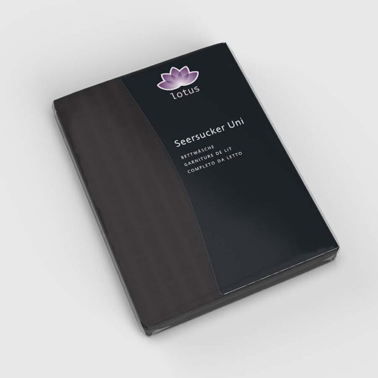 Ein verpacktes Set von Lotus Bettwäsche Satin Seersucker Schwarz hat einen dunklen Einband mit einem lila Lotus-Logo und Text in Englisch, Deutsch und Italienisch. Die Verpackung ist vor einem weißen Hintergrund abgebildet.