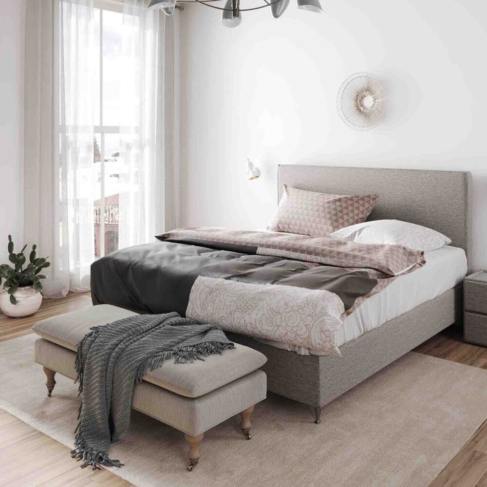 Ein gemütliches, modernes Schlafzimmer mit einem großen Bett mit Bettwäsche Yeshia Lotus Création, einer Bank mit einer Decke am Fußende, einem weichen Teppich, durchsichtigen Vorhängen, die das natürliche Licht hereinlassen, und einem Topfkaktus in der Ecke.