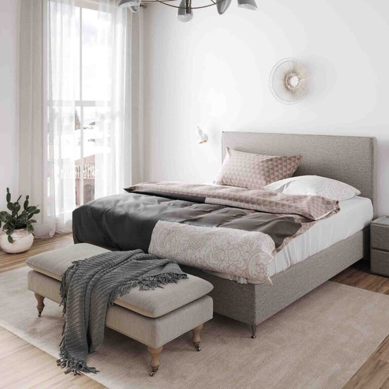 Ein gemütliches, modernes Schlafzimmer mit einem großen Bett mit Bettwäsche Yeshia Lotus Création, einer Bank mit einer Decke am Fußende, einem weichen Teppich, durchsichtigen Vorhängen, die das natürliche Licht hereinlassen, und einem Topfkaktus in der Ecke.