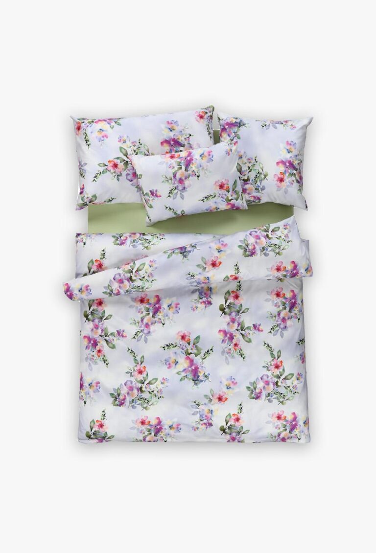 Ein ordentlich arrangiertes Bett mit weißer Bettwäsche Tamara-R Selection Hilda, mit einem farbenfrohen Blumenmuster mit lila, rosa und gelben Blumen sowie grünen Blättern auf dem Bettbezug, zwei großen Kissen und einem kleineren Kissen.