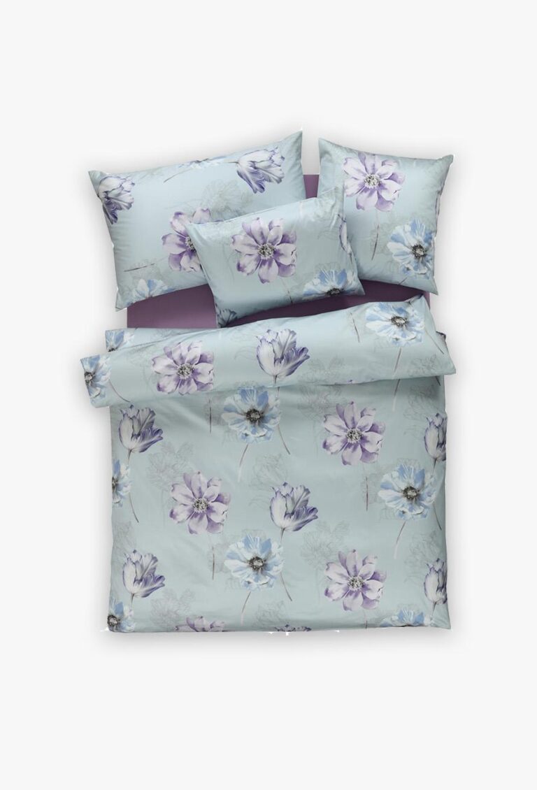 Die Bettwäsche Tamara-R Selection Smilla blau besteht aus einem Bettbezug und vier Kissen mit großen lila und blauen Blumen auf hellblauem Hintergrund, die ordentlich auf einem Bett angeordnet sind.
