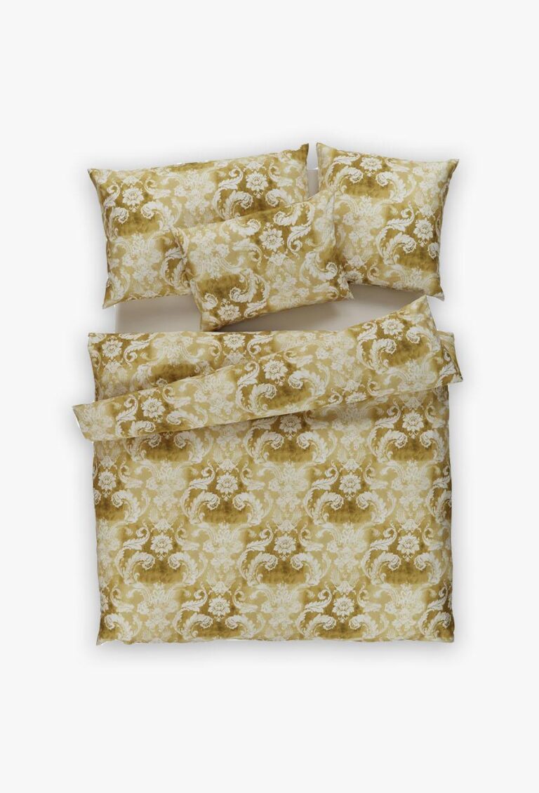 Das Set Bettwäsche Tamara-R Emotion Antico gold besteht aus einem Bettbezug und zwei Kissenbezügen in Goldgelb und Weiß mit einem verschnörkelten Blumenmuster auf weißem Grund.