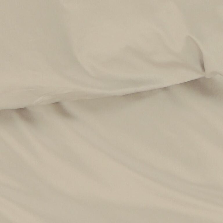 Eine Nahaufnahme von Bettwäsche a beige, einem cremefarbenen Stoff mit sichtbaren Falten und weichen Knitterfalten, die sanfte Schatten erzeugen, der möglicherweise als Bettlaken oder Kopfkissenbezug verwendet wurde.