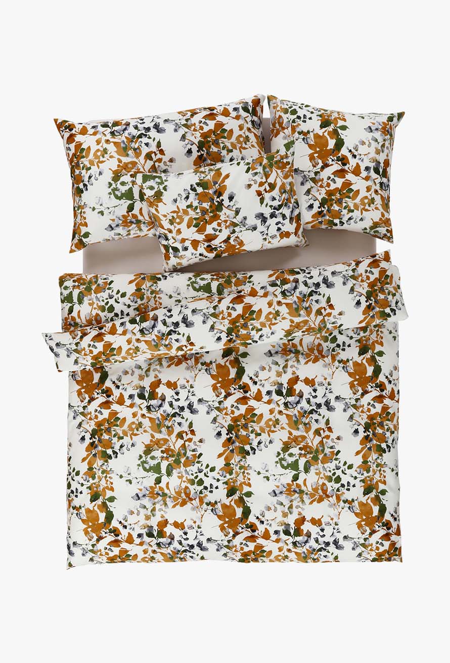 Das Set Bettwäsche Viane besteht aus einem geblümten Bettbezug und Kissenbezügen mit orangefarbenen, grünen und braunen Blättern auf weißem Hintergrund, die ordentlich auf dem Bett angeordnet sind.