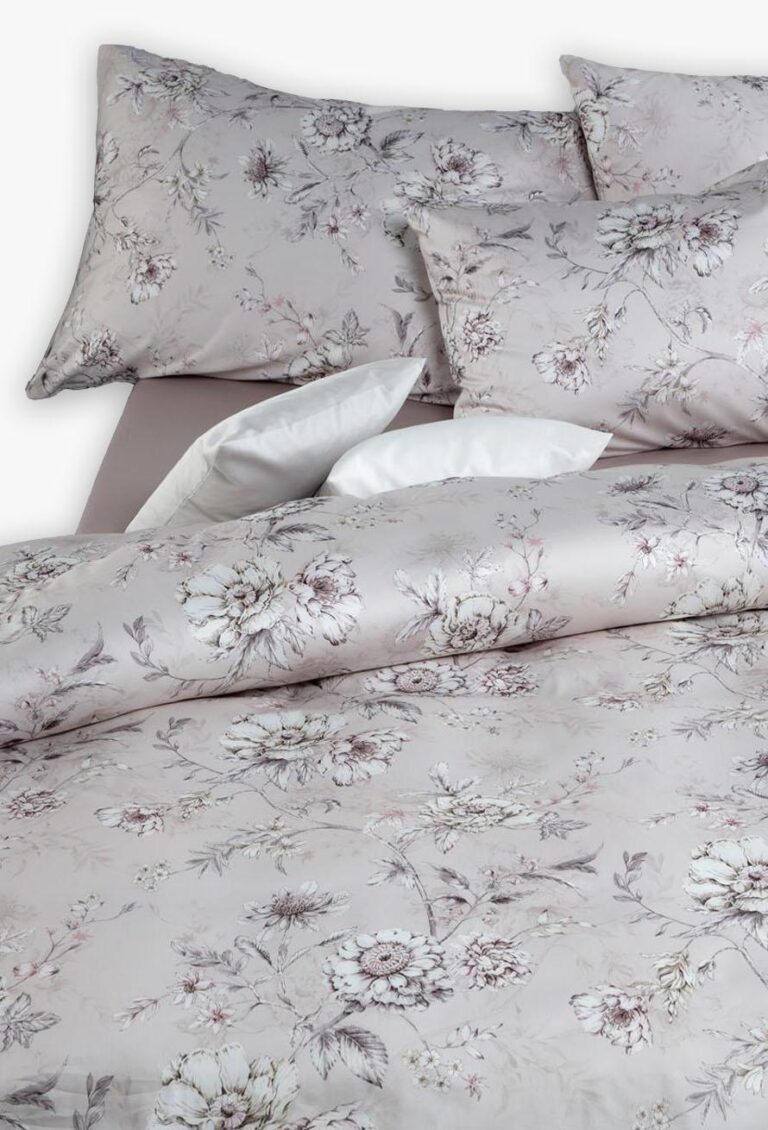 Ein ordentlich gemachtes Bett mit der hellen Bettwäsche Tamara-R Selection Elissa, die ein zartes Blumenmuster in Taupe, Creme und zartem Rosa zeigt, gepaart mit passenden Kissenbezügen und einem weißen Akzent-Kissen.