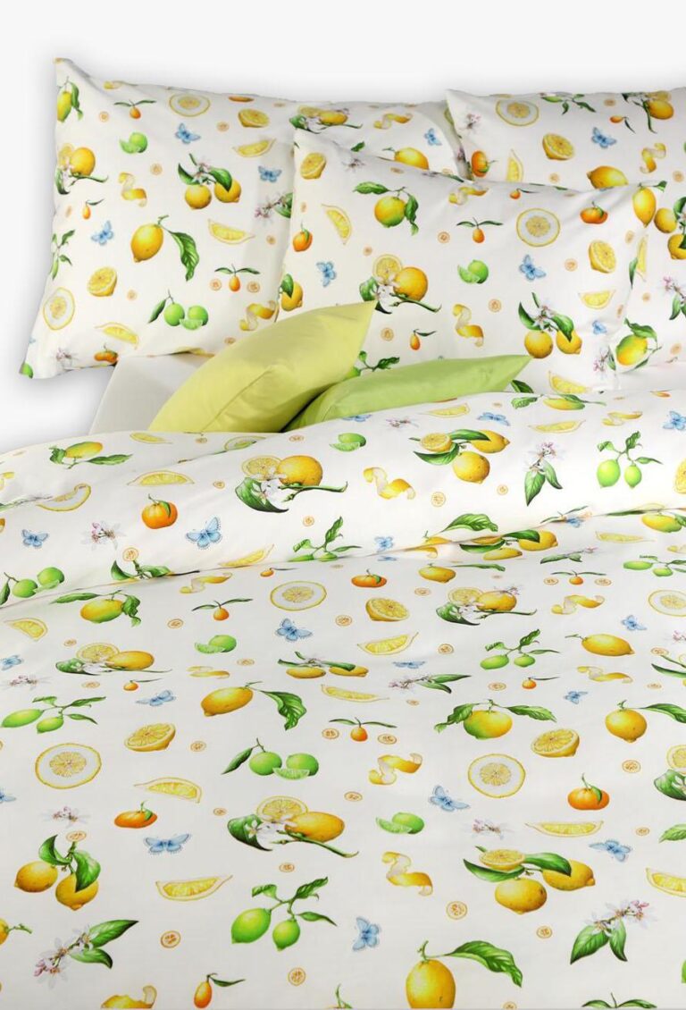Das Bettwäsche-Set Tamara-R Emotion Eva zeigt weiße Bettwäsche mit leuchtenden Zitronen, Orangen, grünen Blättern, blauen Schmetterlingen und rosa Blüten. Ein blassgrünes Laken unter der Bettdecke setzt einen frischen Akzent.