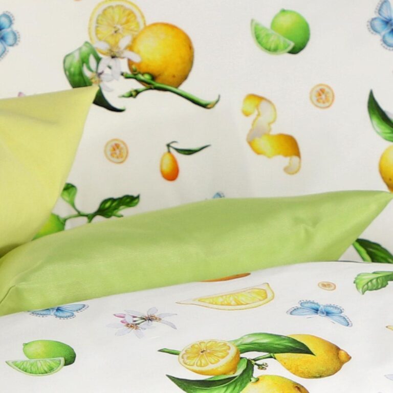 Zwei grüne Kissen ruhen auf einer weißen Bettwäsche Tamara-R Emotion Eva mit Zitronen, Limetten, grünen Blättern, Orangenscheiben, blauen Schmetterlingen und kleinen Blumen auf einem passenden gemusterten Hintergrund.