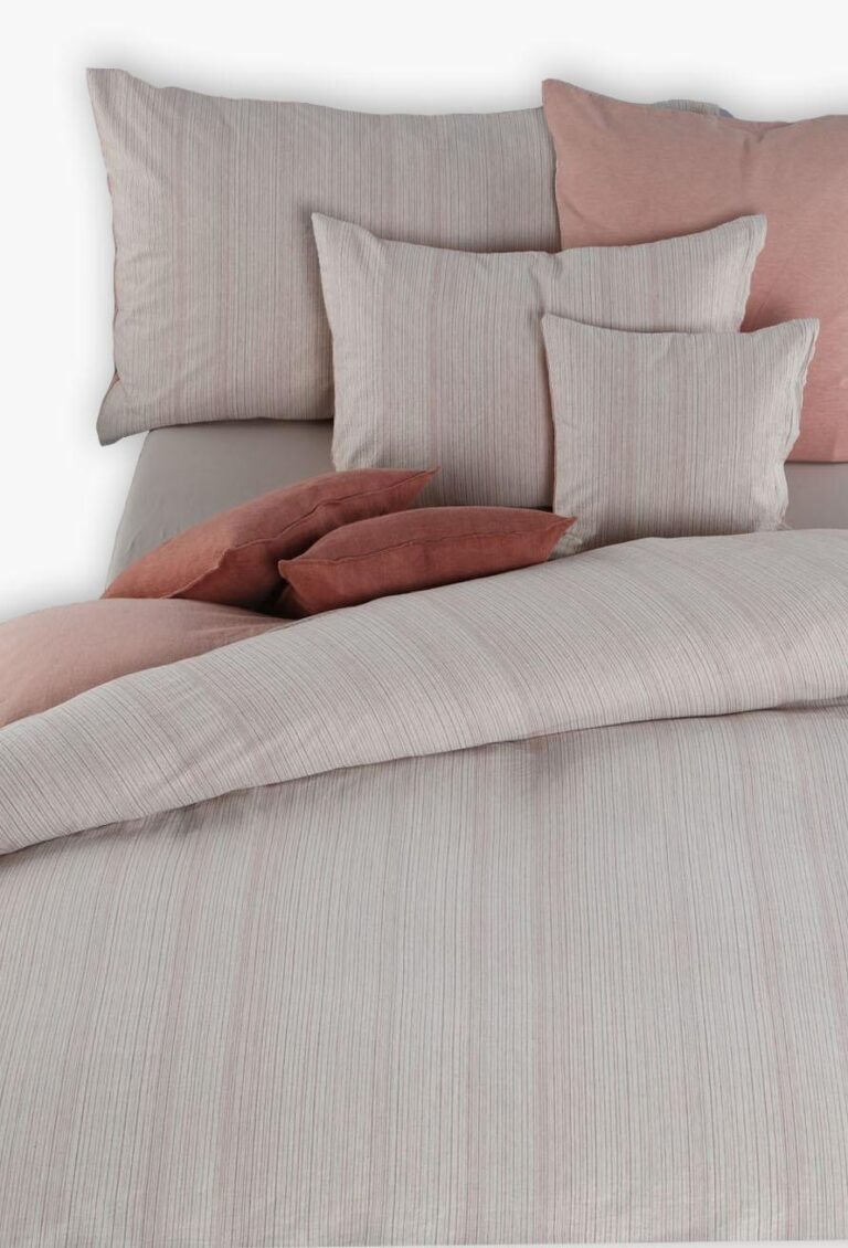 Ein ordentlich gemachtes Bett mit der Bettwäsche Tamara-R BeCosy Flo, mit einem hellbeigen und gestreiften Bettbezug, großen beigen und rosafarbenen Kissen sowie Akzentkissen in Rosa und Rost für einen gemütlichen, einladenden Look.