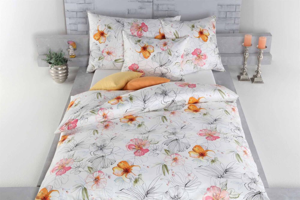 Die Bettwäsche Tamara-R Selection Lotta ist mit einem lebhaften Blumenmuster in Orange, Gelb und Rosa versehen. Obenauf liegen passende Kissen und zwei feste Kissen, und das Kopfteil wird mit Dekoartikeln akzentuiert.