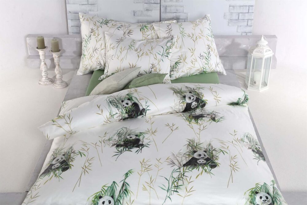Ein Bett mit Bettwäsche Tamara-R Selection Panda zeigt einen Panda- und Bambusdruck, grüne Lakenakzente und passende Kissen. Kerzen und eine weiße Laterne schmücken die Nachttische vor einer weißen Backsteinwand.