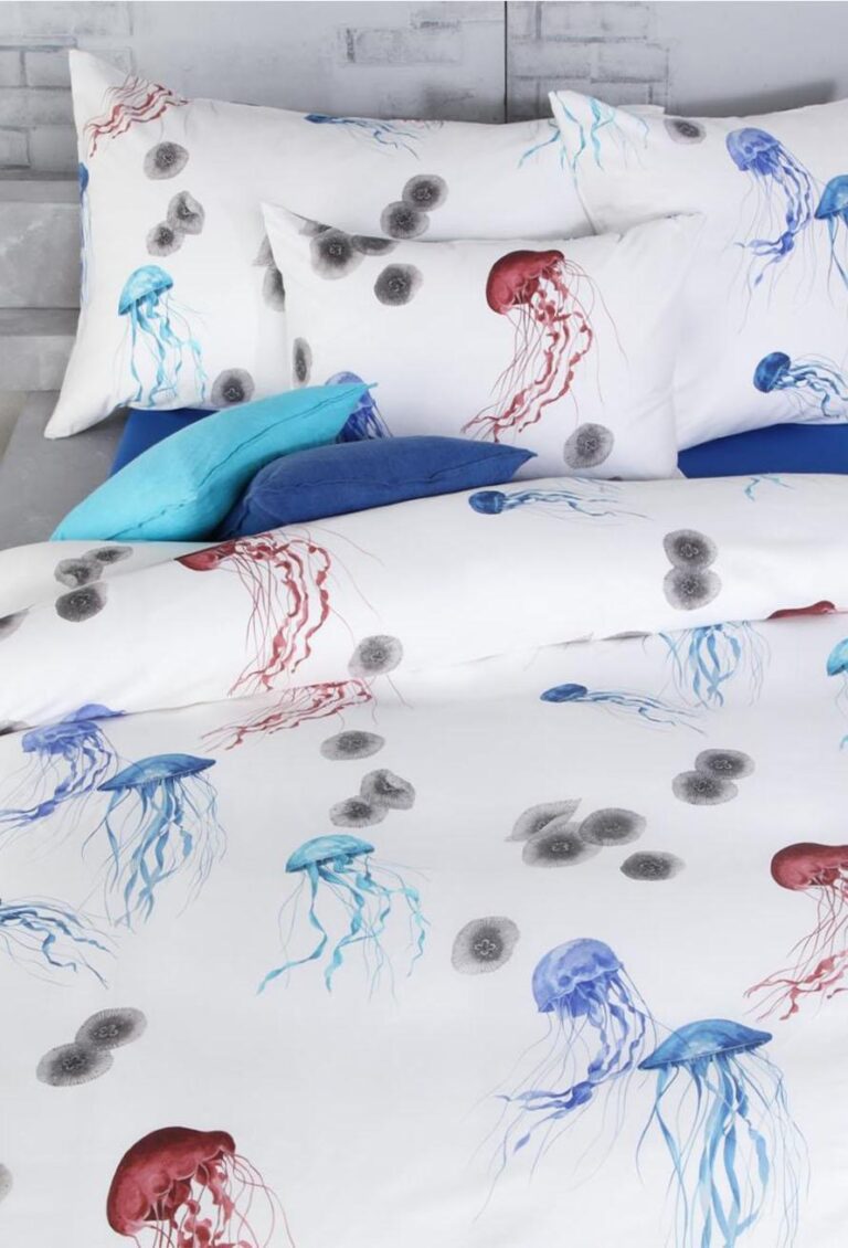 Die Bettwäsche Tamara-R Selection Quallina ist ein weißes Bettwäscheset mit roten und blauen Quallen und grauen Kreisen, ergänzt durch blaue und türkise Akzentkissen auf hellem Grund.