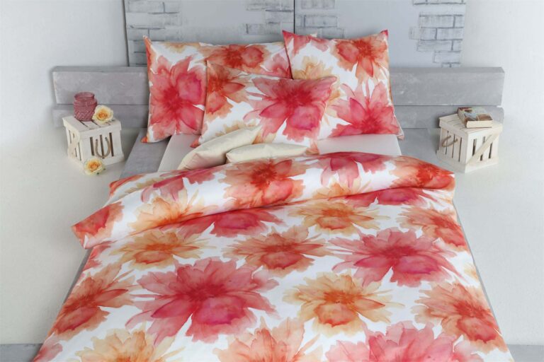 Ein Bett aus Bettwäsche Tamara-R Selection Sofie mit kräftigen roten und orangefarbenen Blumendrucken im Aquarellstil auf Weiß hebt sich von einem grauen Kopfteil ab, umgeben von dekorativen Kisten und Blumen.