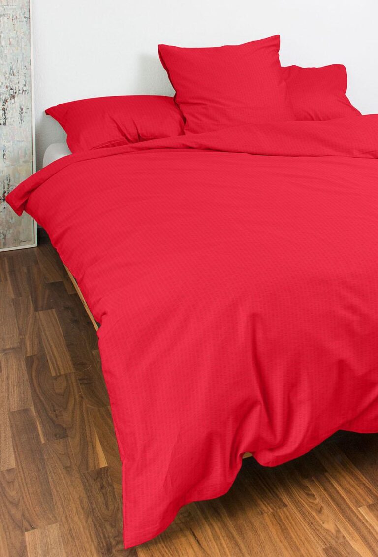 In einem Zimmer mit Holzfußboden und weißer Wand steht ein ordentlich gemachtes Bett mit Bettwäsche Night Fashion Edi in leuchtendem Rot, komplett mit Bettdecke und Kissen.