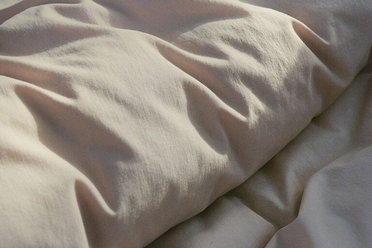 Eine Nahaufnahme von Bettwäsche Journey Living Bellecour mit beigen oder cremefarbenen Laken in weichem natürlichem Licht, das sanfte Schatten auf dem strukturierten, faltigen Stoff hervorhebt.
