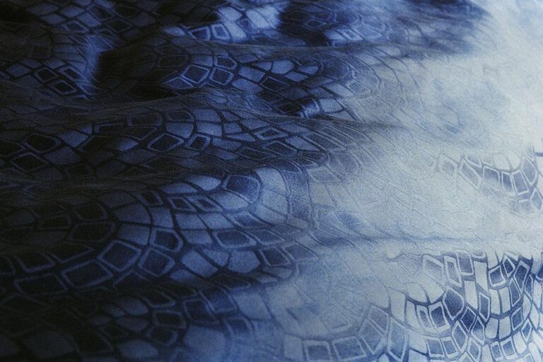 Eine Nahaufnahme der Bettwäsche Journey Living Casablanca zeigt blauen Stoff mit geometrischen, kachelartigen Mustern und weichen, wellenförmigen Schatten auf der strukturierten Oberfläche.