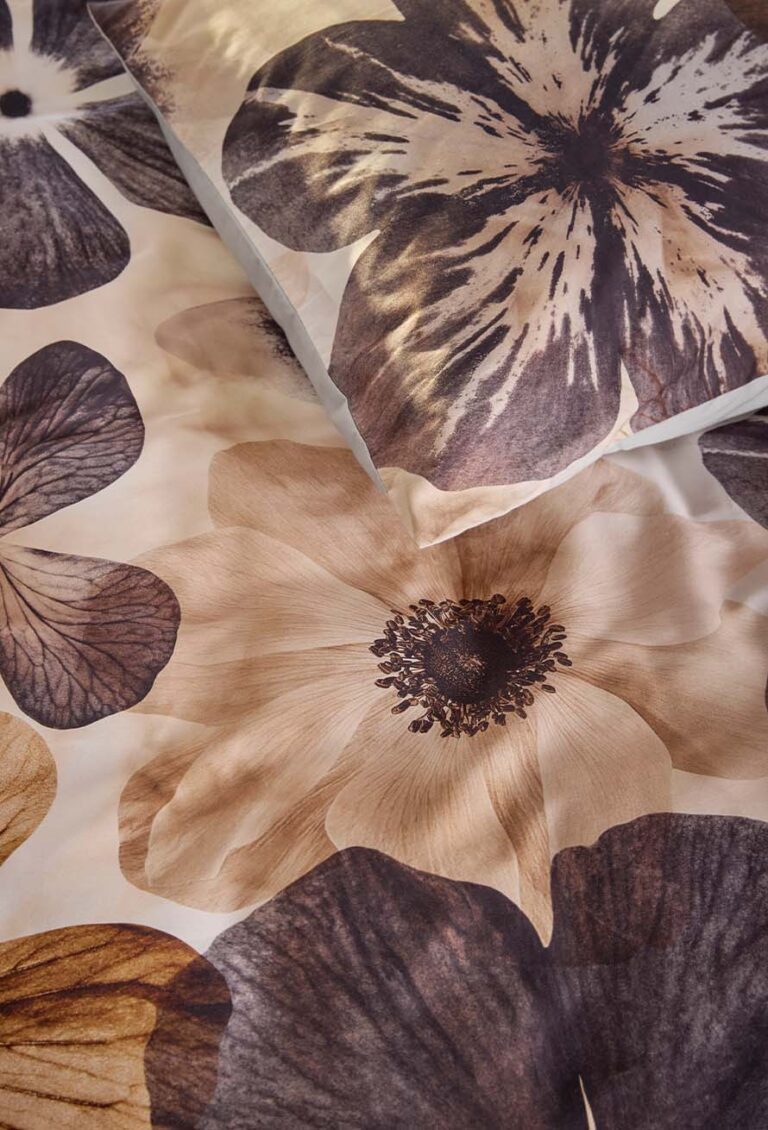 Die Nahaufnahme von Bettwäsche Beddinghouse Jane zeigt große, detaillierte Blumen in Braun, Beige und dunklem Lila auf glattem Stoff. Oben ist ein Teil des Kissens zu sehen.