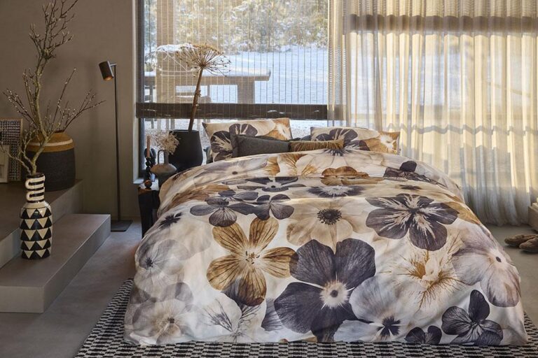 Das gemütliche Schlafzimmer ist mit einem großen Bett mit Bettwäsche von Bettwäsche House Jane ausgestattet, das durch neutrales Dekor, einen gemusterten Teppich und bodentiefe Fenster mit Blick auf die verschneite Natur ergänzt wird.