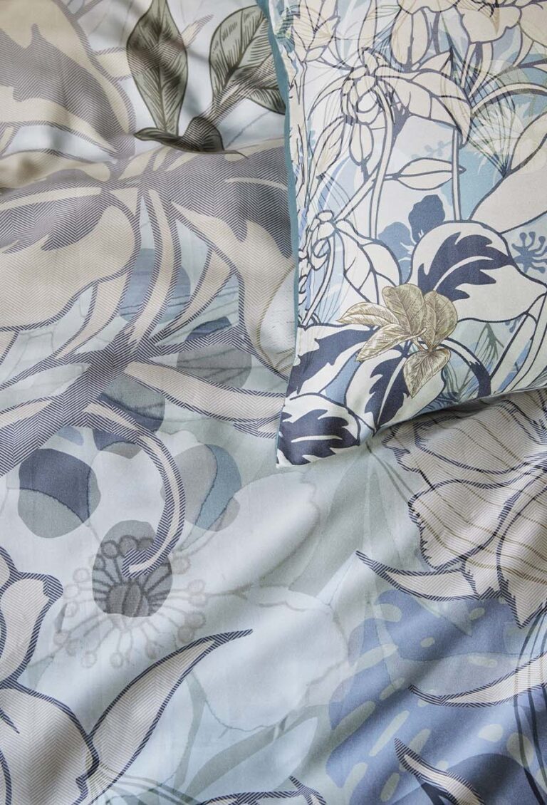 Nahaufnahme eines Bettes, das mit Bettwäsche von Beddinghouse Nobile bezogen ist, mit hellblauer, grauer und beiger Bettwäsche und einem passenden Kissen mit großen abstrakten Blumen- und Blattmustern.
