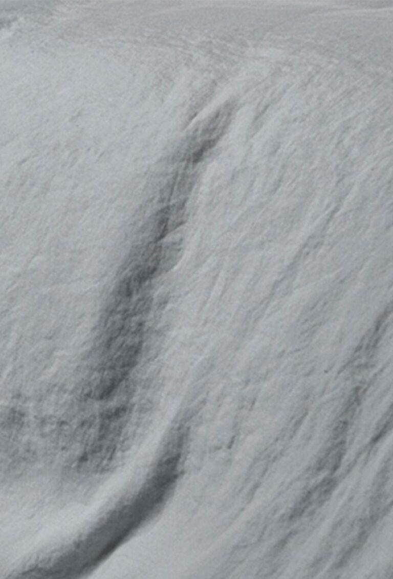 Eine Nahaufnahme von Bettwäsche Tamara-R BeCosy Nico zeigt weiche Falten und Knicke, die zarte Schatten und Texturen auf der hellen Stoffoberfläche erzeugen.