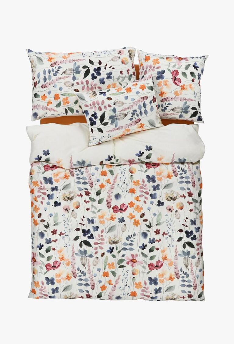 Ein Bett, das mit Bettwäsche Tamara-R Selection Sally bezogen ist, zeigt sein lebhaftes Blumenmuster in Orange, Rosa, Violett und Grün auf einem strahlend weißen Hintergrund auf der Bettdecke, den Kissenbezügen und den Unterbetten.