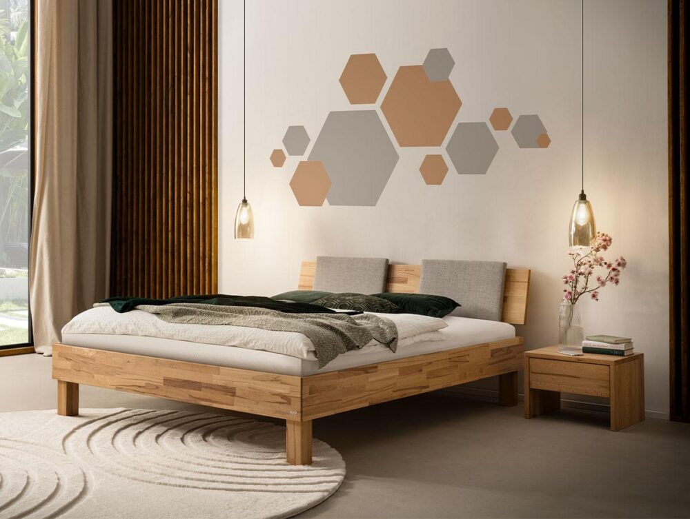 Ein modernes Schlafzimmer mit einem Holzbett, neutraler Bettwäsche, zwei Pendelleuchten, einem kleinen Beistelltisch mit einer Vase und geometrischer Sechseck-Wandkunst in Beige- und Grautönen. Natürliches Licht fällt durch ein Fenster auf der linken Seite ein.
