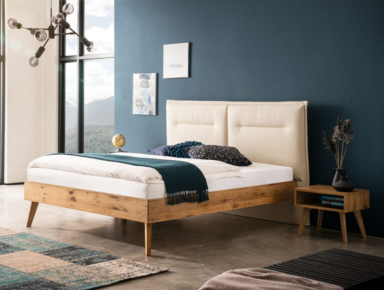 Modernes Schlafzimmer mit einem hölzernen Bettgestell, einem cremefarbenen gepolsterten Kopfteil, einer blaugrünen Decke, Kissen, einem kleinen hölzernen Nachttisch, Dekorationsartikeln, einer dunkelblauen Akzentwand, großen Fenstern und einer modernen Leuchte.