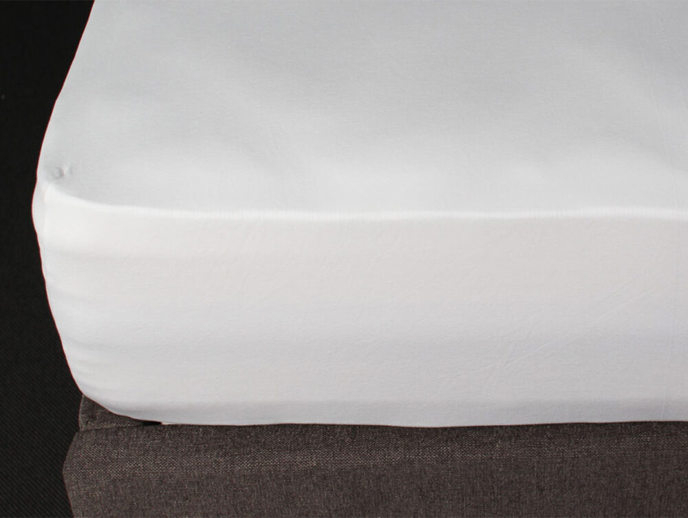 Nahaufnahme eines weißen Spannbettlakens, das die Ecke einer Matratze, die auf einem dunkelgrauen Bettgestell liegt, sauber abdeckt.