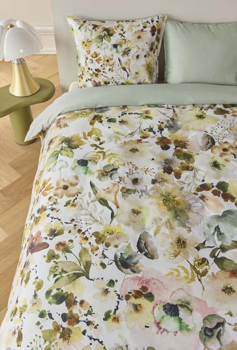 Ein Bett mit Bettwäsche Beddinghouse Aquitaine - eine blumengemusterte Bettdecke und Kissen in Grün, Gelb und Braun - steht neben einem grünen runden Beistelltisch mit einer modernen weißen Lampe auf einem Holzboden.